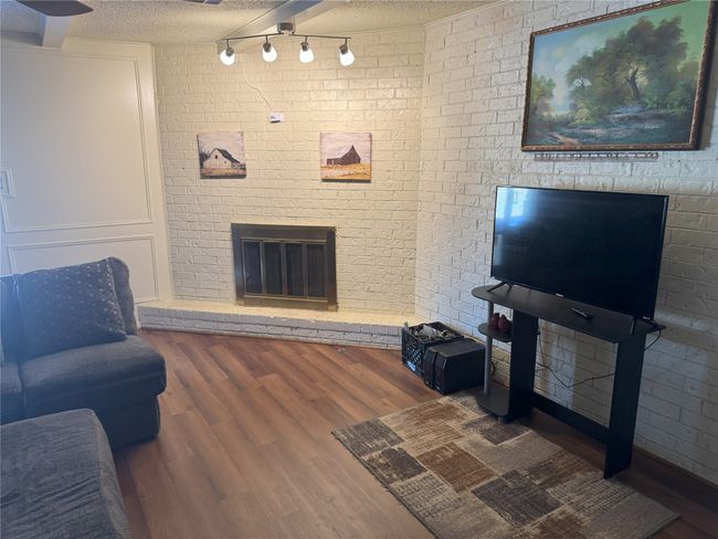 Living room with hardwood / wood-style floors, a textured ceiling, brick wall, and a brick fireplace | Image 10