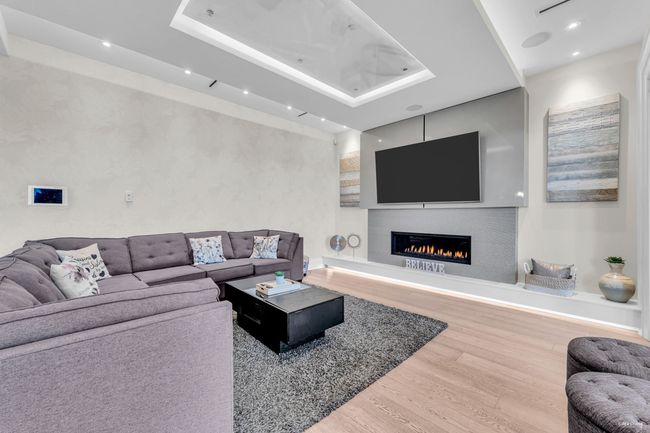 Living room with wood finished floors, recessed lighting, a lit fireplace, and a tray ceiling | Image 25