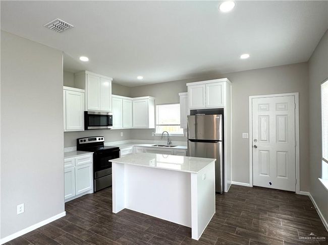 Kitchen featuring stainless steel appliances, white cabinets, a sink, dark wood finished floors, and light countertops | Image 5