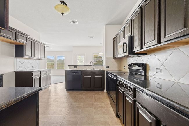 Kitchen featuring black appliances, a sink, dark brown cabinets, a peninsula, and backsplash | Image 19