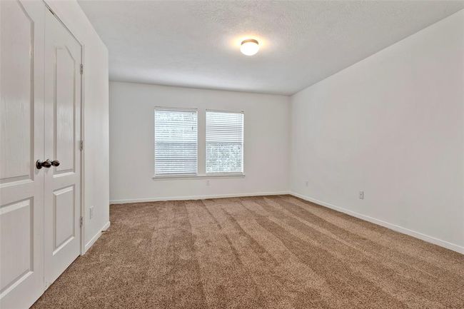This is a spacious, carpeted bedroom featuring neutral walls, double doors, and two large windows that allow natural light to fill the room. Ideal for a bedroom or an office. | Image 23