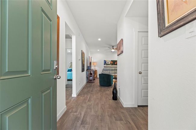 The green front door opens to a bright, welcoming interior featuring LVP flooring in a natural wood color, which adds warmth and character to the space. The white walls create a clean, modern backdrop, while sleek, modern baseboards add a touch of refinement. Straight ahead, the hallway leads into the living room, offering an inviting space for relaxation and socializing. | Image 4