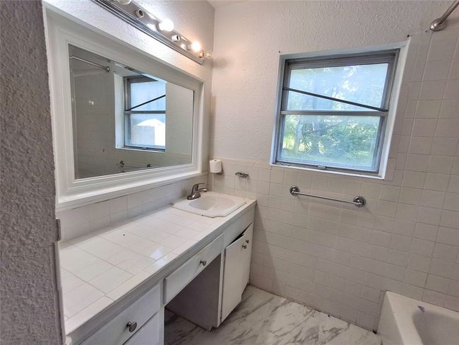 Full bath featuring plenty of natural light, vanity, marble finish floors, a textured wall, and tile walls | Image 21