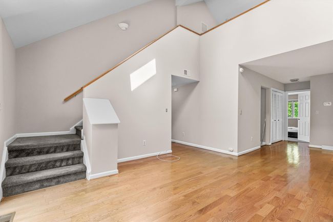 Unfurnished living room featuring stairway, light wood-style flooring, baseboards, and a towering ceiling | Image 5