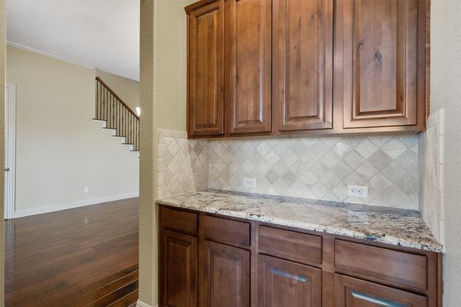 Kitchen with backsplash, light stone countertops, ornamental molding, dark wood-style flooring, and brown cabinetry | Image 23
