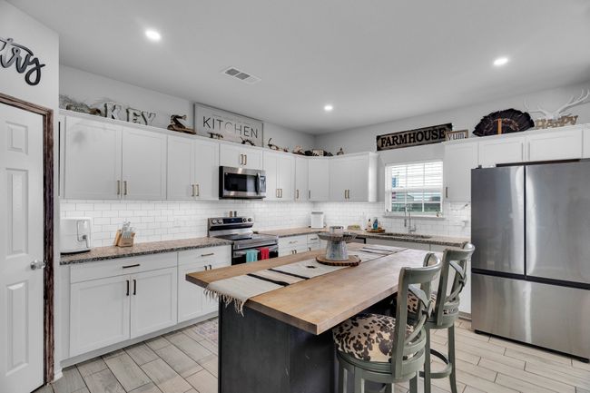Kitchen with stainless steel appliances, butcher block countertops, white cabinets, tasteful backsplash, and recessed lighting | Image 5