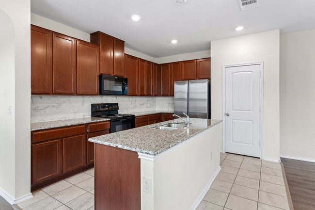Kitchen with black appliances, light tile patterned floors, light stone countertops, tasteful backsplash, and recessed lighting | Image 7