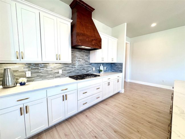 Kitchen with custom range hood, stainless steel gas stovetop, backsplash, white cabinetry, and recessed lighting | Image 11