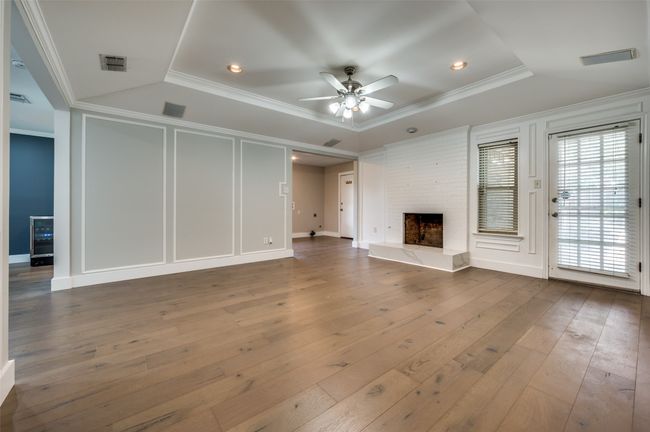 Unfurnished living room featuring ornamental molding, hardwood / wood-style floors, ceiling fan, a fireplace, and a tray ceiling | Image 8