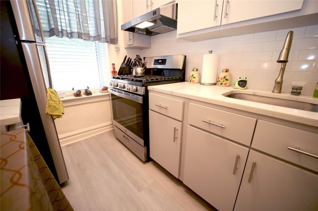 Kitchen featuring stainless steel gas range oven, under cabinet range hood, a sink, light wood-style flooring, and decorative backsplash | Image 7