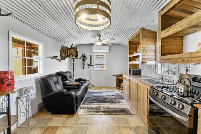 Kitchen featuring stainless steel gas stove, a wall unit AC, a ceiling fan, stone finish flooring, and a sink | Image 7
