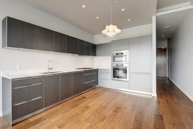 Kitchen with a sink, stainless steel appliances, light countertops, modern cabinets, and light wood-style flooring | Image 7