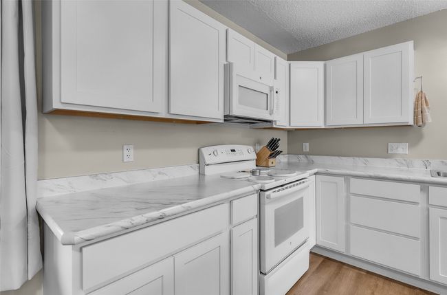 Kitchen with white appliances, white cabinetry, a textured ceiling, and light wood-type flooring | Image 15