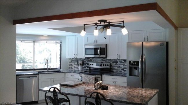 Kitchen with dark stone counters, decorative backsplash, white cabinets, a sink, and stainless steel appliances | Image 4