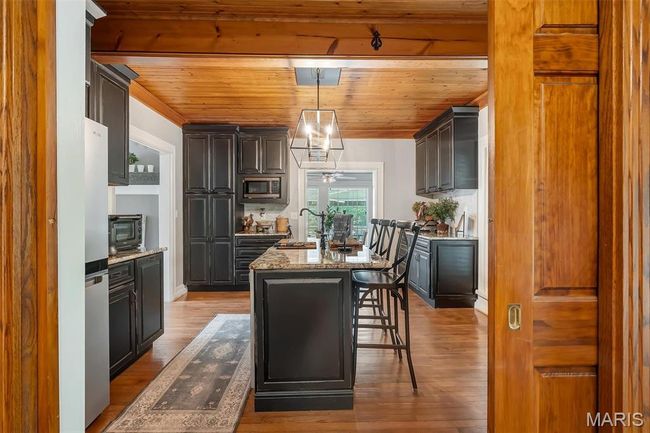 Kitchen with stainless steel appliances, wood ceiling, a center island with sink, light stone countertops, and wood finished floors | Image 49