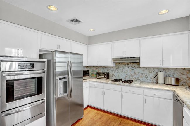 Kitchen featuring white cabinets, decorative backsplash, light stone counters, stainless steel appliances, and light hardwood / wood-style flooring | Image 15