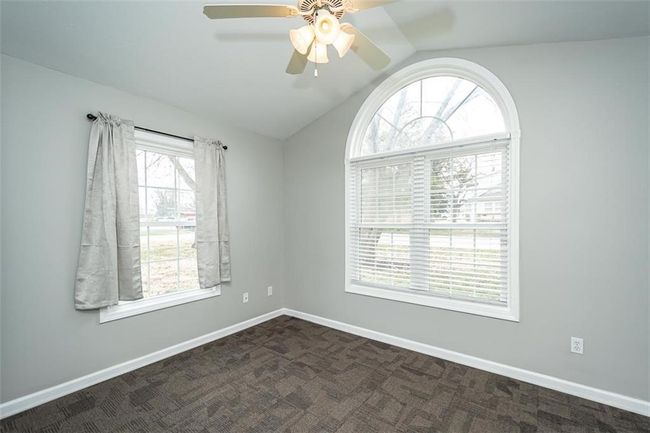 Unfurnished room featuring lofted ceiling, a ceiling fan, baseboards, and dark colored carpet | Image 32