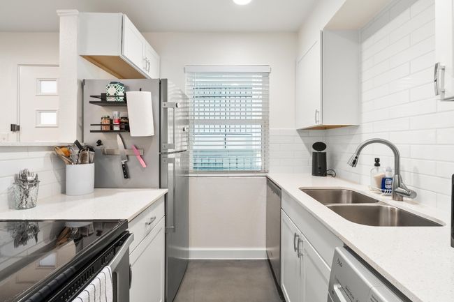 Kitchen featuring decorative backsplash, light stone counters, white cabinetry, and stainless steel dishwasher | Image 6