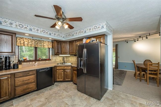 Kitchen featuring stainless steel fridge with ice dispenser, black dishwasher, a sink, a ceiling fan, and light countertops | Image 12