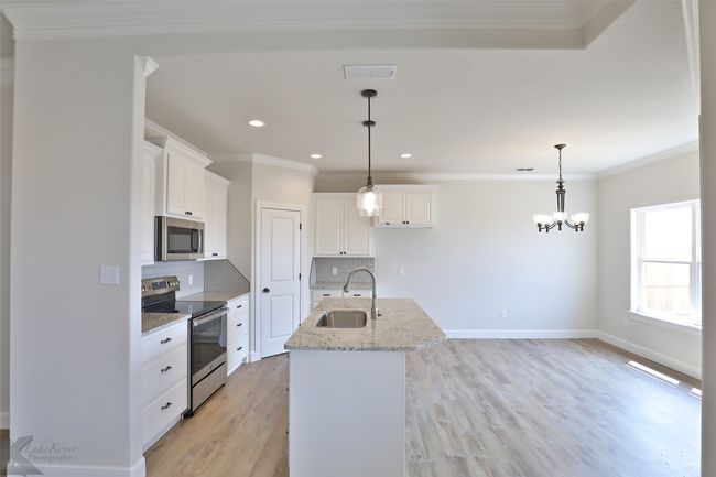 Kitchen featuring stainless steel appliances, decorative backsplash, light wood-style flooring, crown molding, and white cabinetry | Image 11