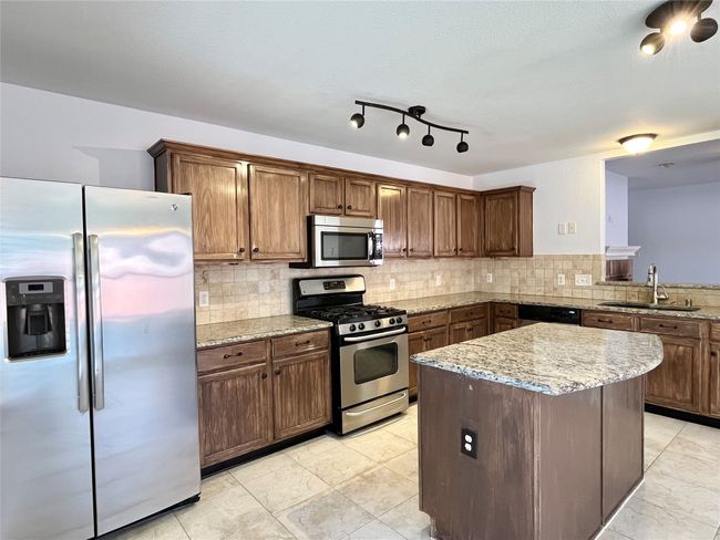 Kitchen with stainless steel appliances, light stone counters, a kitchen island, and tasteful backsplash | Image 6