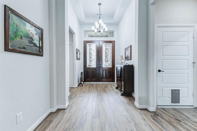 Another view of the entryway showcases the elegant double doors, a tray ceiling, and a stunning light fixture. From this vantage point, you’ll also notice access to the garage as well as the convenient placement of the guest bedroom and bathroom. | Image 4