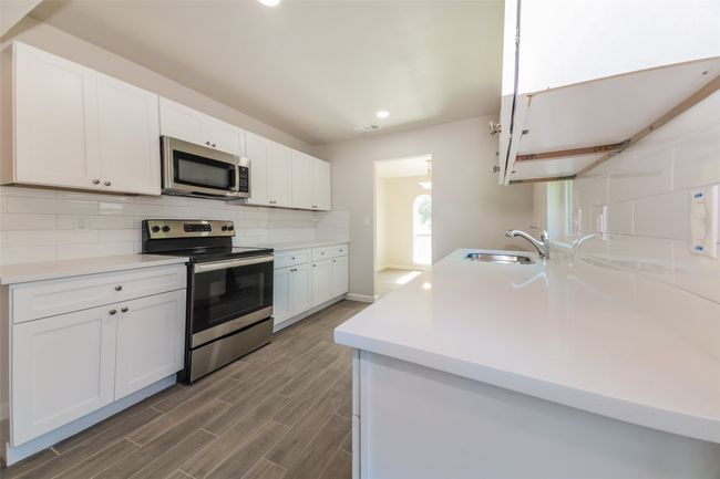 Kitchen featuring stainless steel appliances, tasteful backsplash, recessed lighting, white cabinets, and wood finished floors | Image 13