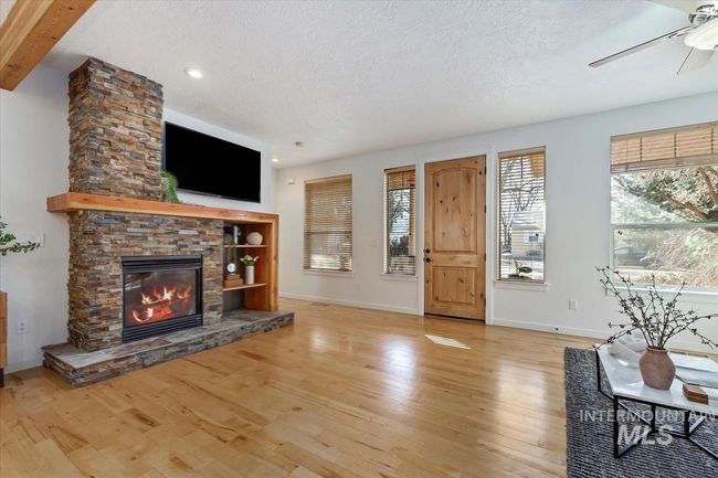 Unfurnished living room with a textured ceiling, healthy amount of natural light, wood finished floors, a fireplace, and beamed ceiling | Image 13