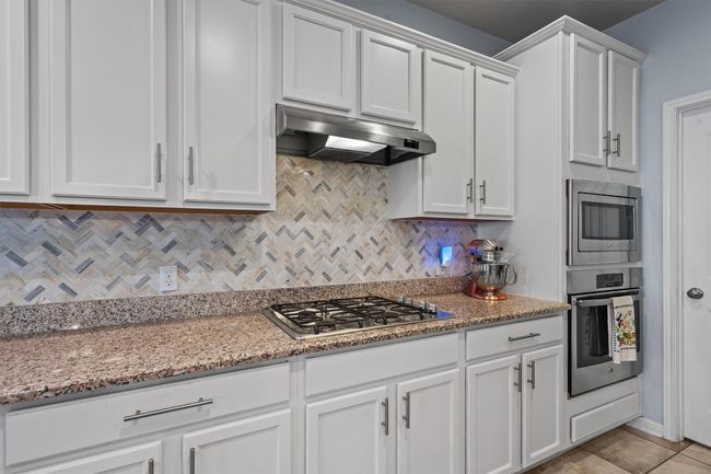 Kitchen featuring stainless steel appliances, under cabinet range hood, white cabinets, backsplash, and light stone counters | Image 15