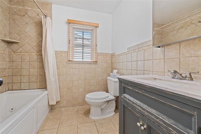 Full bathroom with shower / bath combo, tile patterned floors, vanity, tile walls, and toilet | Image 27