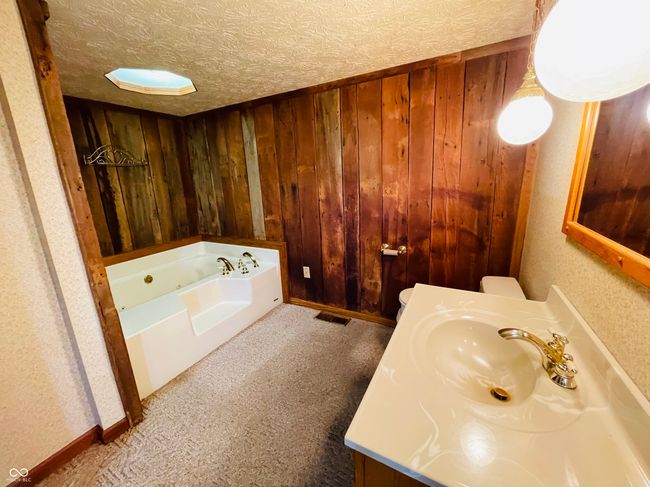 bathroom with a jetted tub, wooden walls, and vanity | Image 23