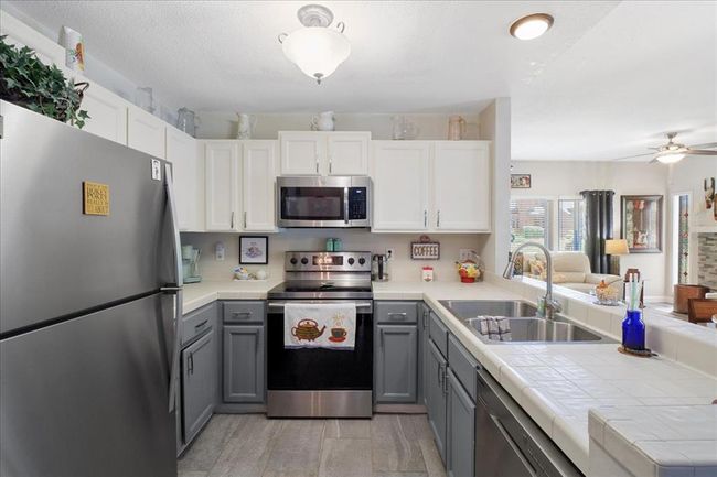 Kitchen with appliances with stainless steel finishes, tile countertops, gray cabinets, white cabinets, and a sink | Image 8