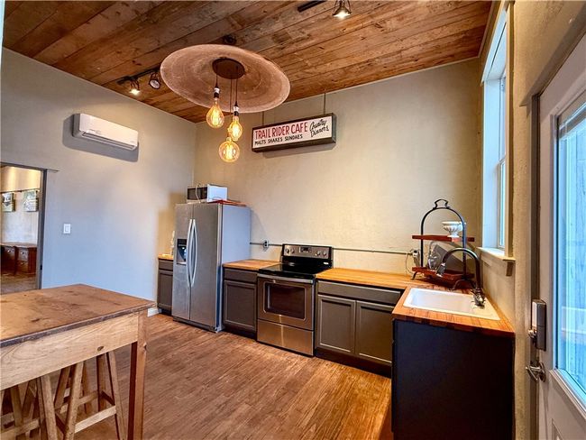 Kitchen with butcher block countertops, wood ceiling, sink, stainless steel appliances, and a wall mounted air conditioner | Image 7