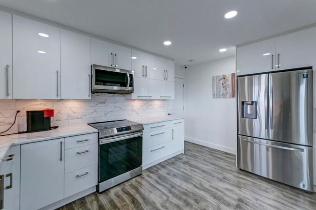Kitchen with stainless steel appliances, light wood-style floors, light stone countertops, baseboards, and white cabinetry | Image 9