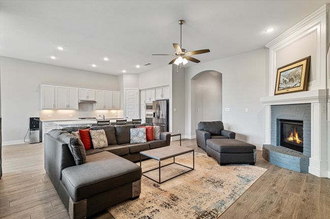 Living area with a ceiling fan, a fireplace, light wood-style floors, baseboards, and arched walkways | Image 5
