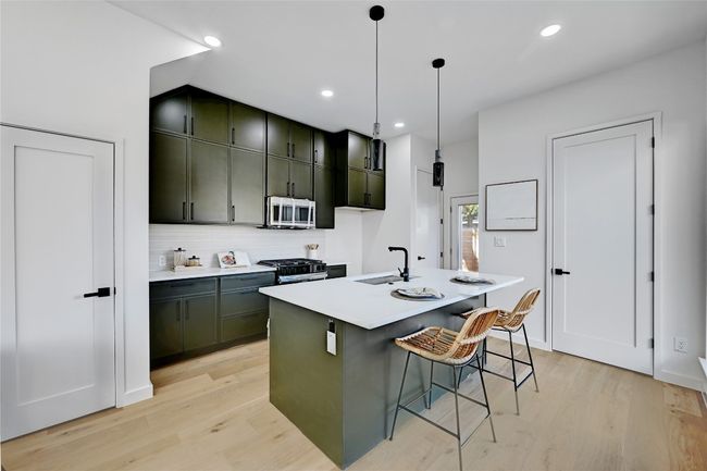 Kitchen with pendant lighting, light hardwood / wood-style floors, sink, a kitchen breakfast bar, and a center island with sink | Image 7