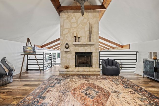 Living area upstairs with high vaulted ceiling, wood finished floors, beam ceiling, and a stone fireplace | Image 35