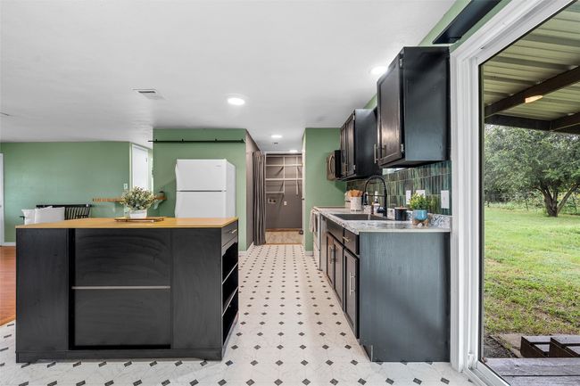 Kitchen featuring freestanding refrigerator, light floors, a center island, wooden counters, and dark cabinetry | Image 9