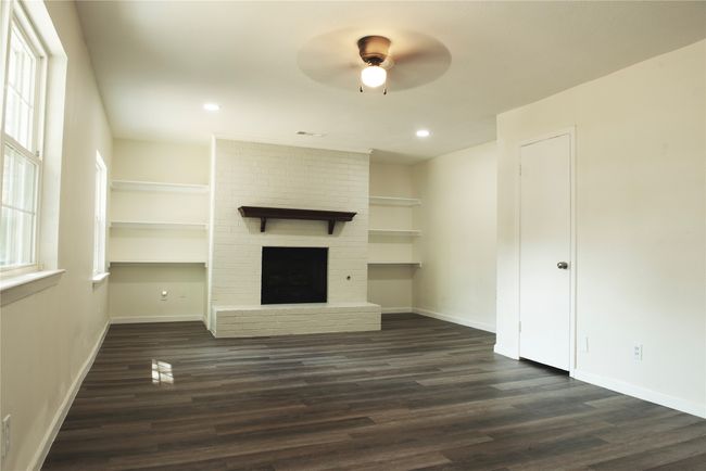 Unfurnished living room with ceiling fan, dark hardwood / wood-style floors, brick wall, and a brick fireplace | Image 4