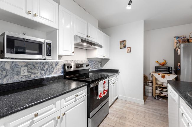 Kitchen featuring under cabinet range hood, appliances with stainless steel finishes, white cabinetry, light wood finished floors, and dark stone counters | Image 11