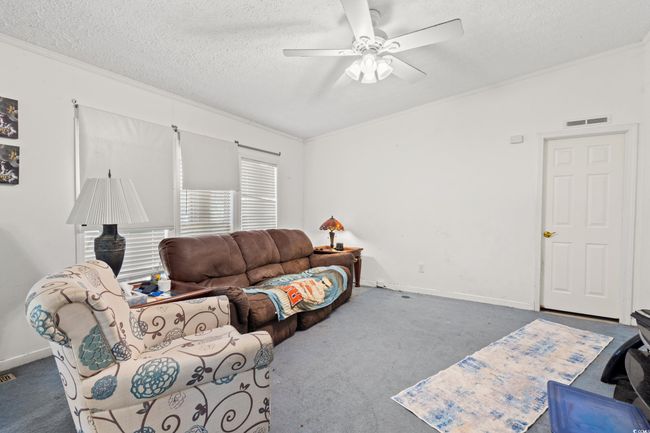 Living area with a textured ceiling, a ceiling fan, crown molding, and carpet floors | Image 5