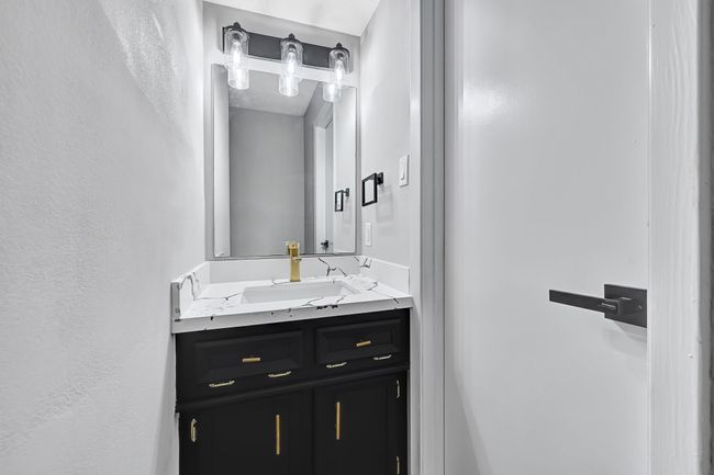 This stylish half bath, conveniently located near the utility room, features an updated vanity with striking black cabinetry, elegant quartz countertops, and a sleek gold faucet—perfectly blending form and function. | Image 33