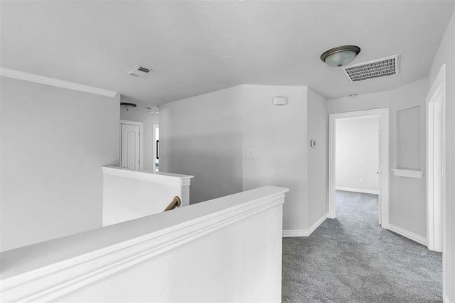 This photo shows a bright, open hallway with neutral-colored walls, carpeted flooring, and multiple doorways leading to other rooms, creating a spacious and inviting upper-level area. | Image 25