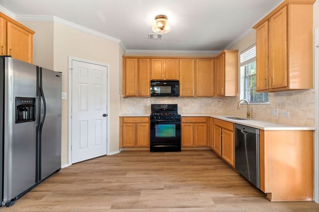 Kitchen featuring a sink, light wood-type flooring, visible vents, light countertops, and black appliances | Image 13