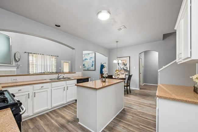 Kitchen featuring arched walkways, black range with gas cooktop, white cabinets, light countertops, and a sink | Image 17