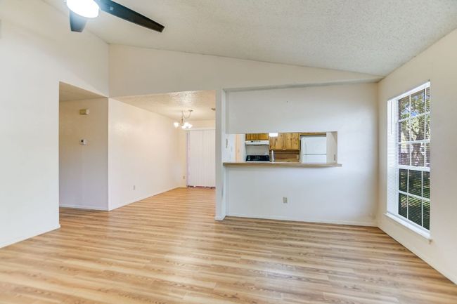 Unfurnished living room with vaulted ceiling, a chandelier, light wood-type flooring, a textured ceiling, and baseboards | Image 4