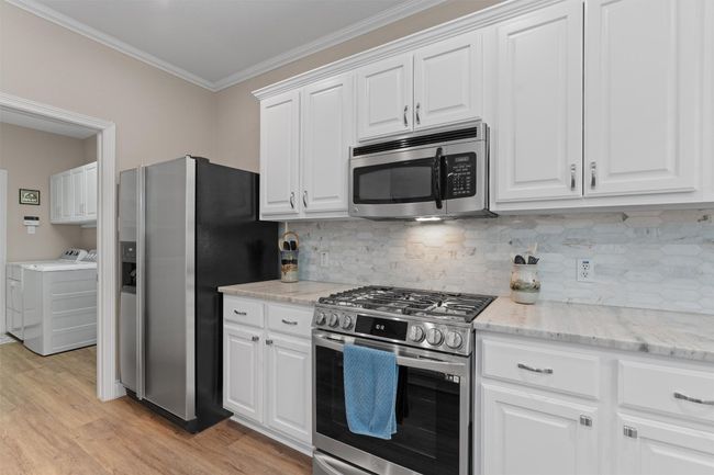 Kitchen with appliances (fridge conveys) with stainless steel finishes, washer and dryer, crown molding, light wood-style flooring, and white cabinetry | Image 12