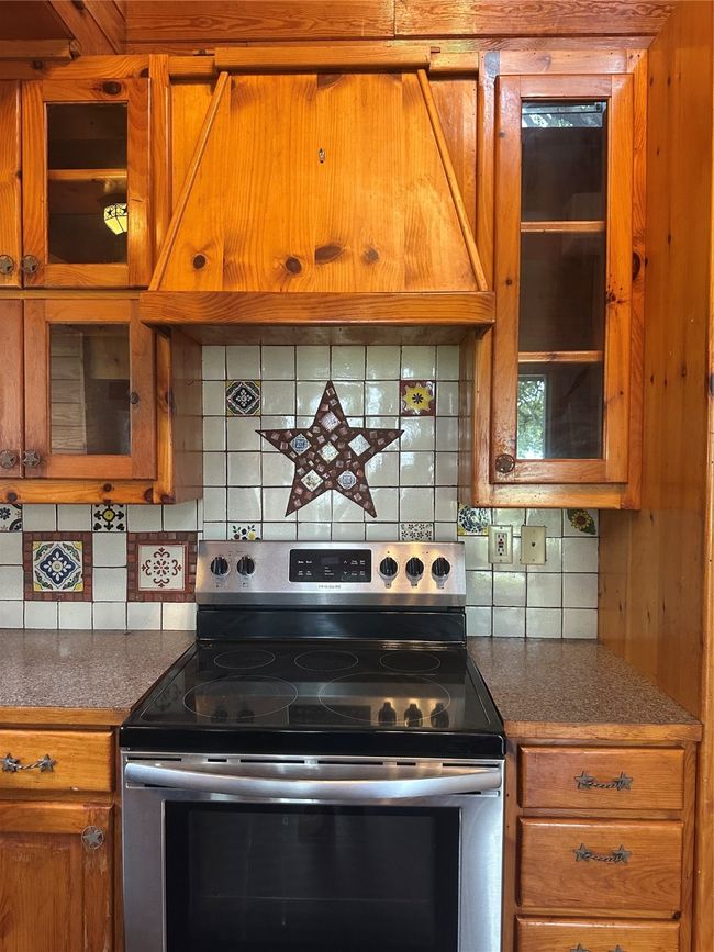 Kitchen with stove, brown cabinets, backsplash, glass insert cabinets, and range hood | Image 7