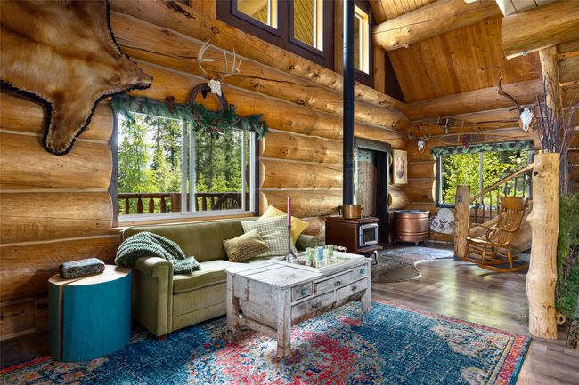 Living area with rustic walls, a wood stove, wooden ceiling with exposed beams, high vaulted ceiling, and wood finished floors | Image 15