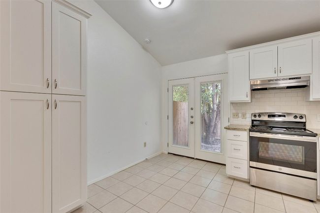 Kitchen featuring stainless steel range with electric cooktop, vaulted ceiling, backsplash, under cabinet range hood, and white cabinets | Image 12